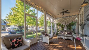 Eine überdachte Veranda mit Korbmöbeln, großen Fenstern und einem Deckenventilator.