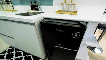 Una cocina compacta con refrigerador integrado, un lavamanos y una encimera con cristalería y un juego de cuchillos.