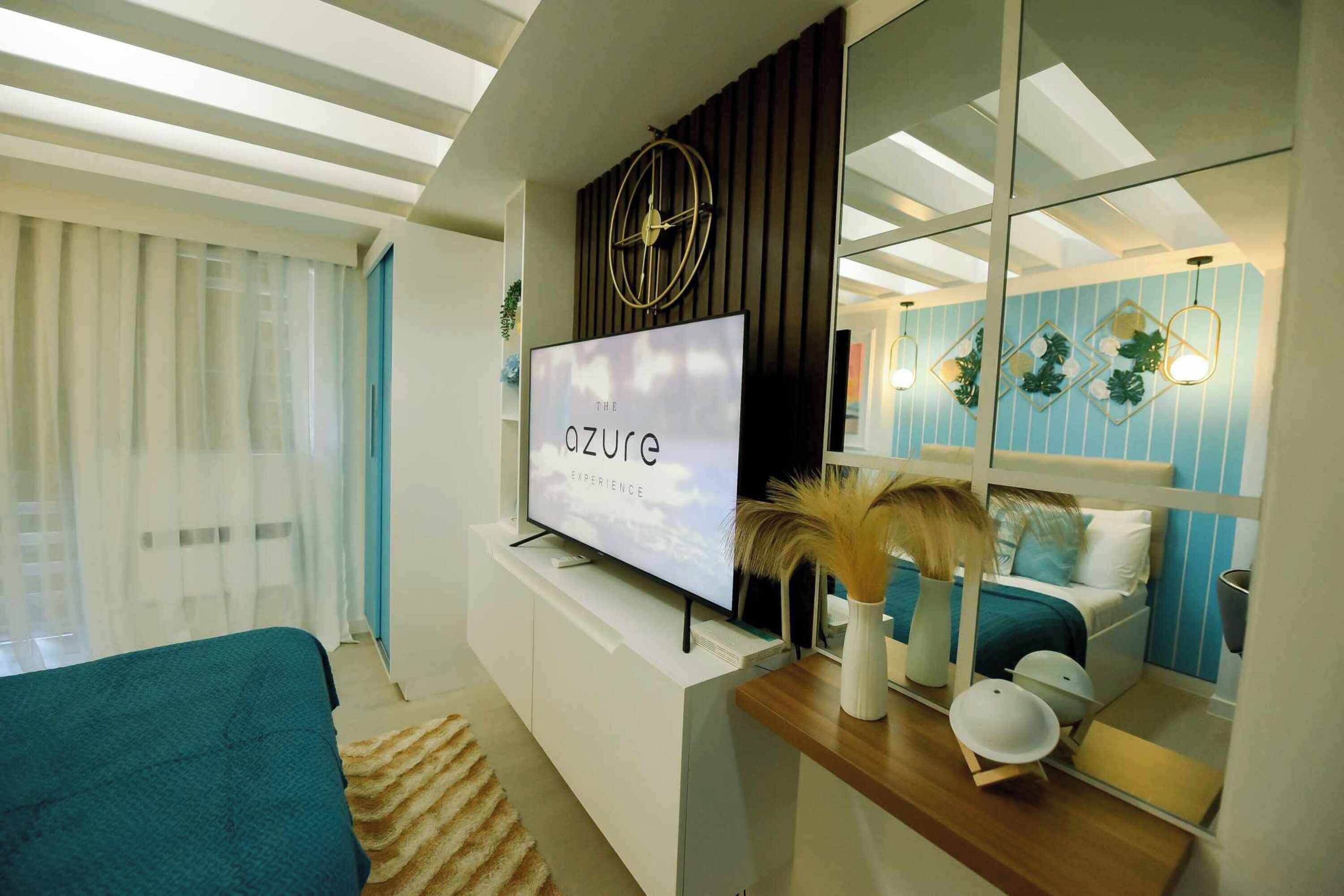 A modern living room with a flat-screen TV, a large mirror, and a bed with a blue and white color scheme.