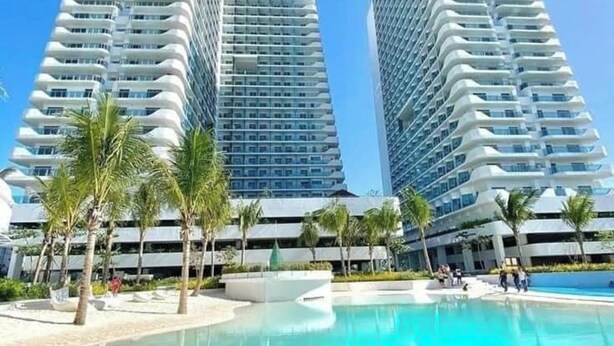 A modern hotel with two high-rise buildings, a clear pool, and palm trees. - Ethan's Crib at Azure North (San Fernando)