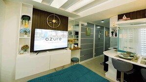 A modern living room with a large flat-screen TV mounted on a white wall, a ceiling fan, and a small table with a bowl and glass. - Ethan's Crib at Azure North (San Fernando)