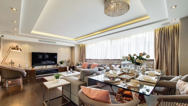 A modern living room with a large flat-screen TV, comfortable seating, a dining area with a glass table, and a chandelier. - The Portman Residences (London)