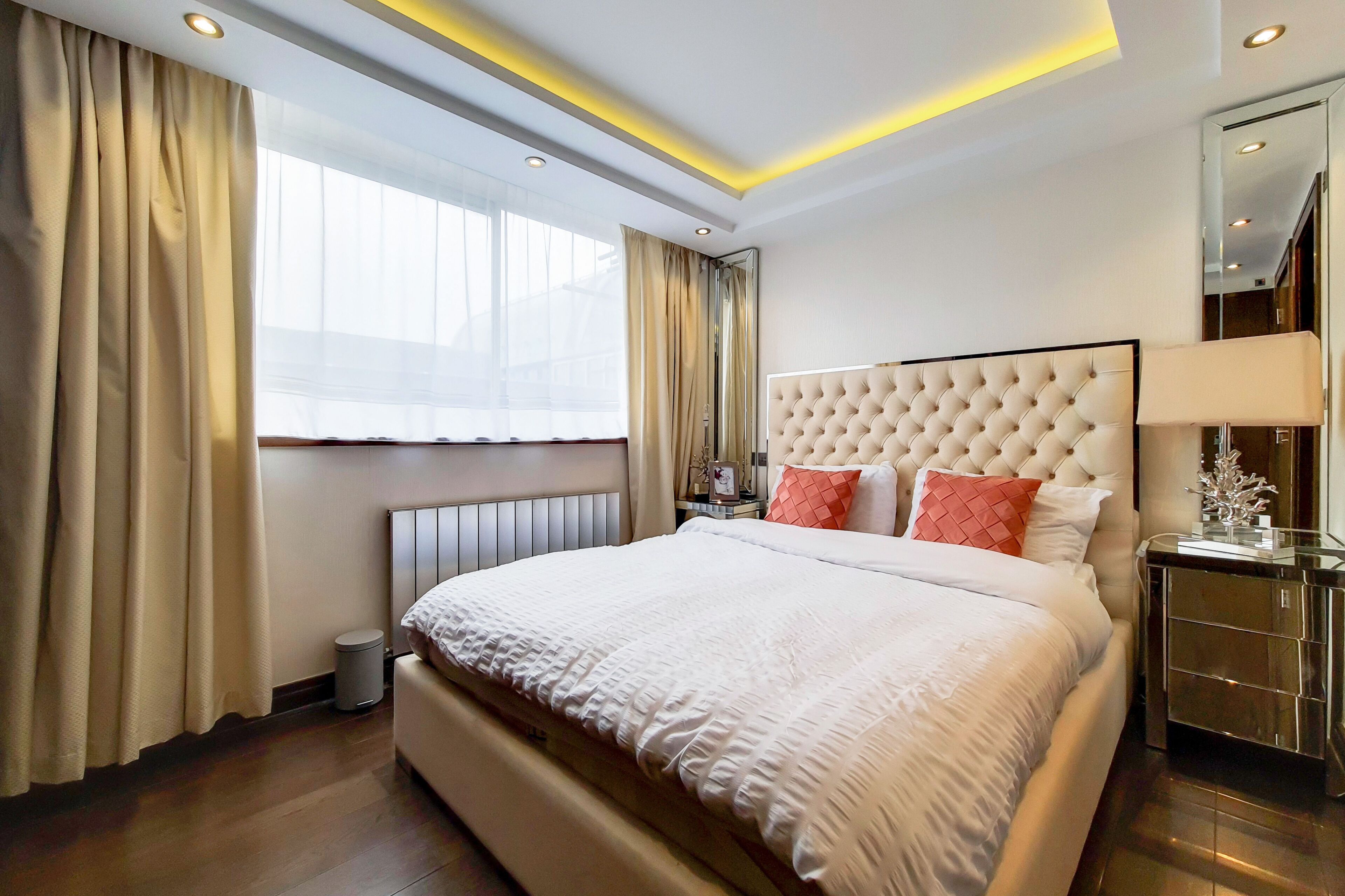 Una habitación de hotel moderna con una cama grande, una mesita de noche, un espejo y una ventana con cortinas.