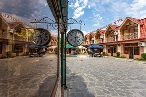 A hotel with a stone-paved courtyard, multiple balconies, and hanging clocks. - Hotel Dimasi (Kutaisi)