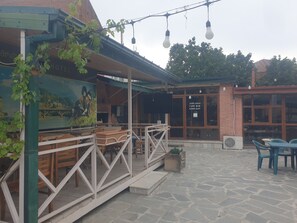 An outdoor seating area with tables and chairs, a mural on the wall, and a sign for a cafe bar. - Hotel Dimasi (Kutaisi)