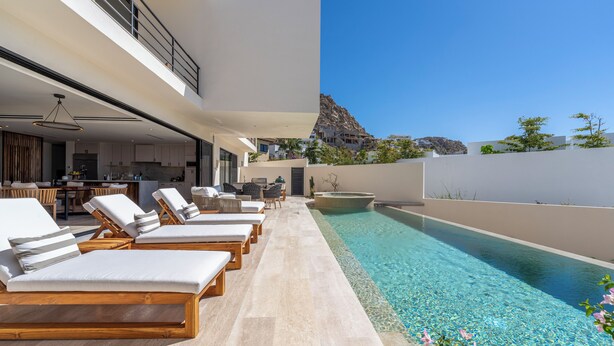 A modern outdoor pool area with lounge chairs, a kitchen, and a view of a mountain. - Amazing Beach View , Walk to the Beach. Cleaning & Concierge (Cabo San Lucas)