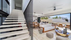 A modern interior with a staircase, a living area with a sofa, coffee table, and dining setup. - Amazing Beach View , Walk to the Beach. Cleaning & Concierge (Cabo San Lucas)