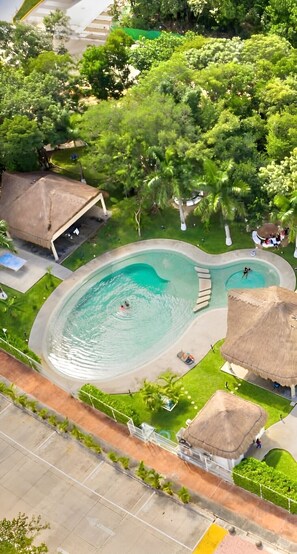 Vista aérea de un resort con una amplia piscina rodeada de exuberante vegetación y chozas con techo de paja.