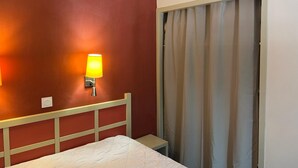 A hotel room with a bed, a nightstand, a wall-mounted lamp, and a window with curtains. - Comfortable apartment in Cannes (Cannes)