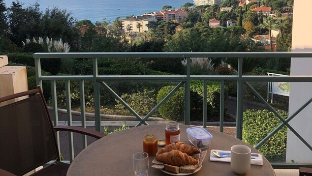 A balcony with a table set for breakfast, overlooking a coastal town with buildings and mountains in the distance. - Comfortable apartment in Cannes (Cannes)