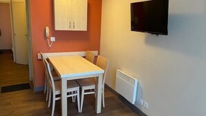A room with a wooden table and chairs, a white cabinet, a wall-mounted TV, and a radiator. - Comfortable apartment in Cannes (Cannes)