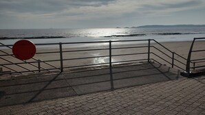 A beach with a metal railing and a red sign. - Meridian Tower Apartment (Swansea)