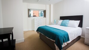 A bedroom with a bed, a desk, a chair, a window, and a nightstand. - Meridian Tower Apartment (Swansea)