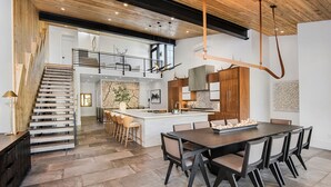 A spacious kitchen with a central island, a dining area with a large table and chairs, and a staircase leading to an upper level. - Sequoia Chalet | 5BR Vail Luxury Retreat, AC, Hot Tub, Views (Vail)