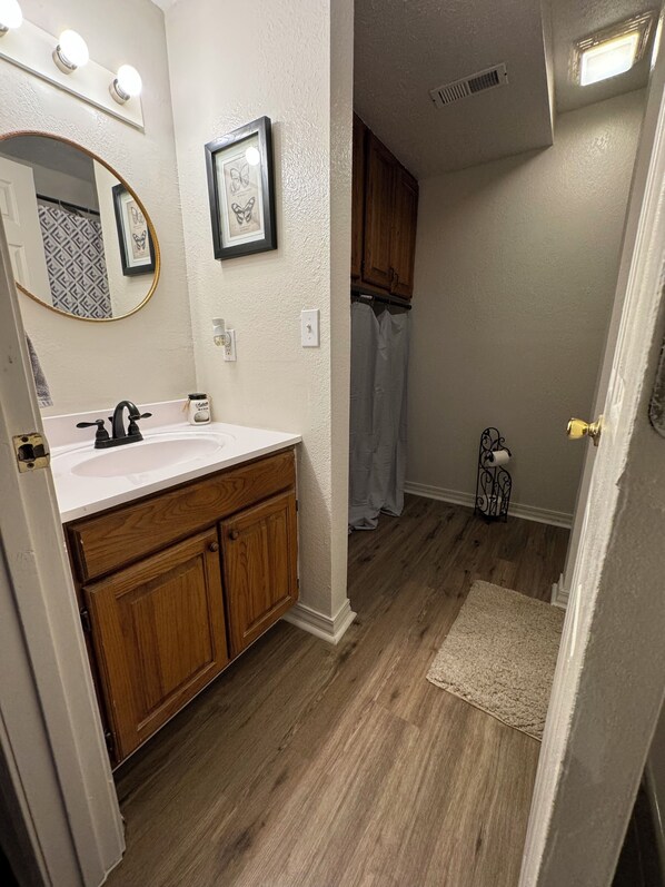 A bathroom with a wooden vanity, a white sink, a mirror with lights, a framed picture, and a shower curtain. - Near Spring River, 2-BR Condo #4 Downtown Hardy (Hardy)