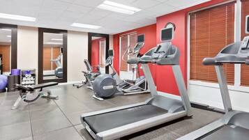 Une salle de sport équipée de tapis de course, de vélos elliptiques et d’un banc de musculation.