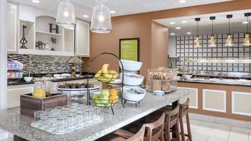 Un espace moderne pour le petit-déjeuner dans un hôtel, avec un comptoir en marbre, divers plats proposés et des lampes suspendues décoratives.