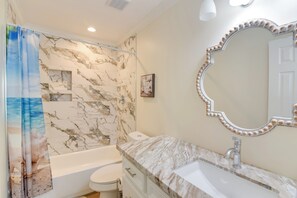 Ein Badezimmer mit Marmorwand, einer Badewanne, einer Toilette, einem Waschbecken mit Spiegel und einer Duschvorhang mit Strandmotiv.