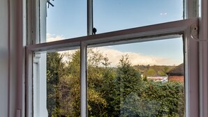 A window with a view of a garden and a distant building. - Spring Cottage (Endon)