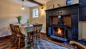 A dining area with a fireplace, wooden chairs, a table set for four, and a patterned rug. - Spring Cottage (Endon)