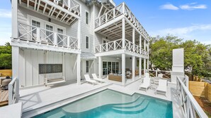 A two-story house with a swimming pool, outdoor seating, and a covered patio area. - Loaded Designer Home with Gulf and Lake Views, Elevator, Heated Pool, and More (Santa Rosa Beach)