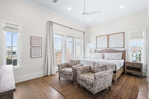 Une chambre à coucher avec un grand lit, deux fauteuils, une table de chevet et une fenêtre avec des rideaux.