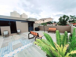 A rooftop patio with a patterned floor, outdoor seating, and a large umbrella.