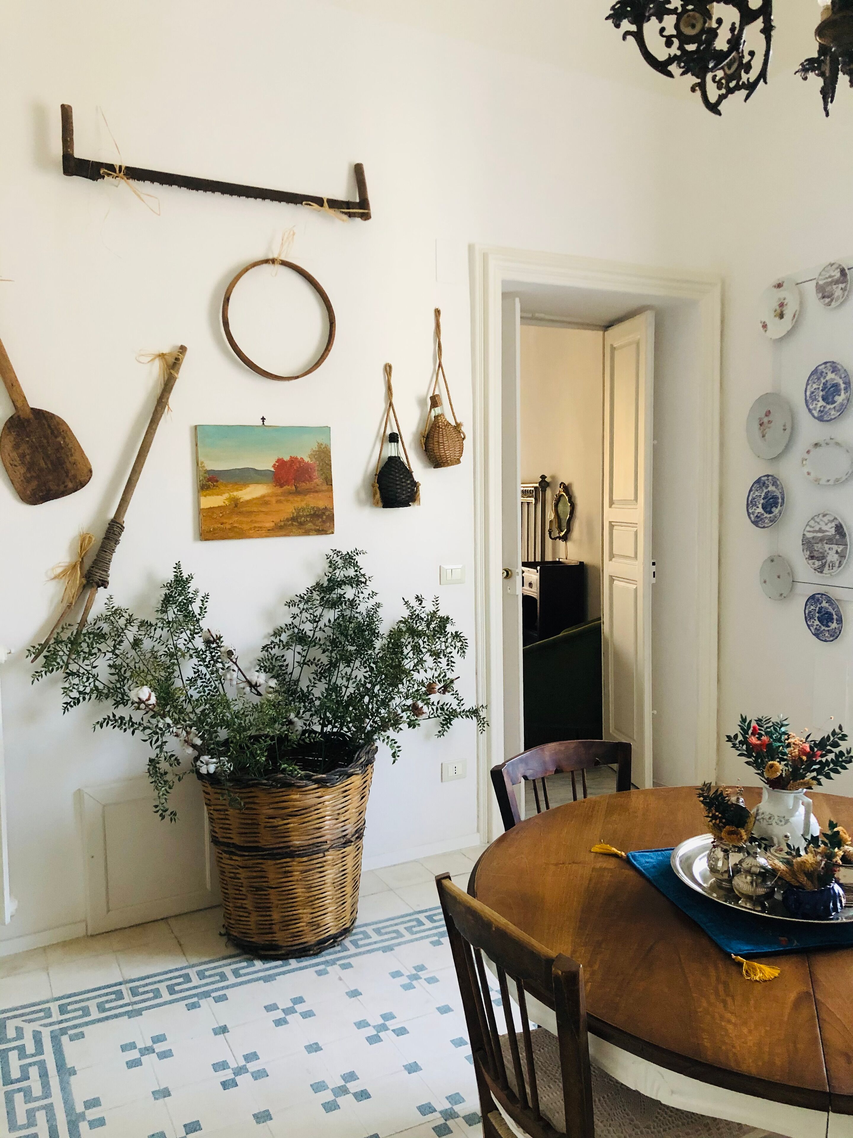 A dining area with a round wooden table, a woven basket with a plant, and a painting on the wall.