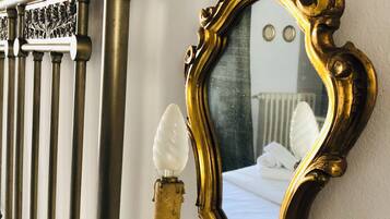 A bed with white linens, a gold-framed mirror, and a white light fixture on a wall.