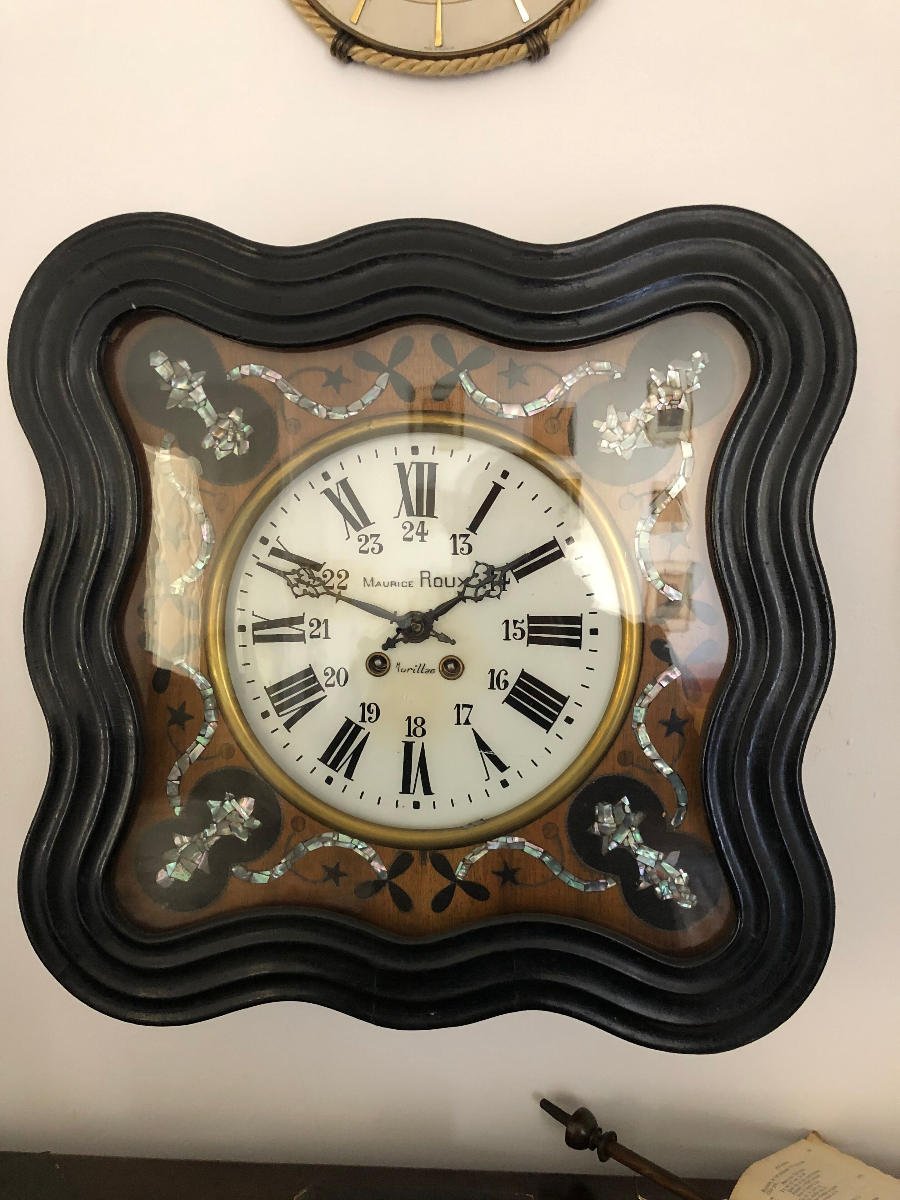 Een aan de muur bevestigd horloge met een decoratieve lijst en Romeinse cijfers.