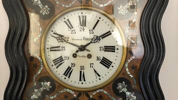 Een aan de muur bevestigd horloge met een decoratieve lijst en Romeinse cijfers.