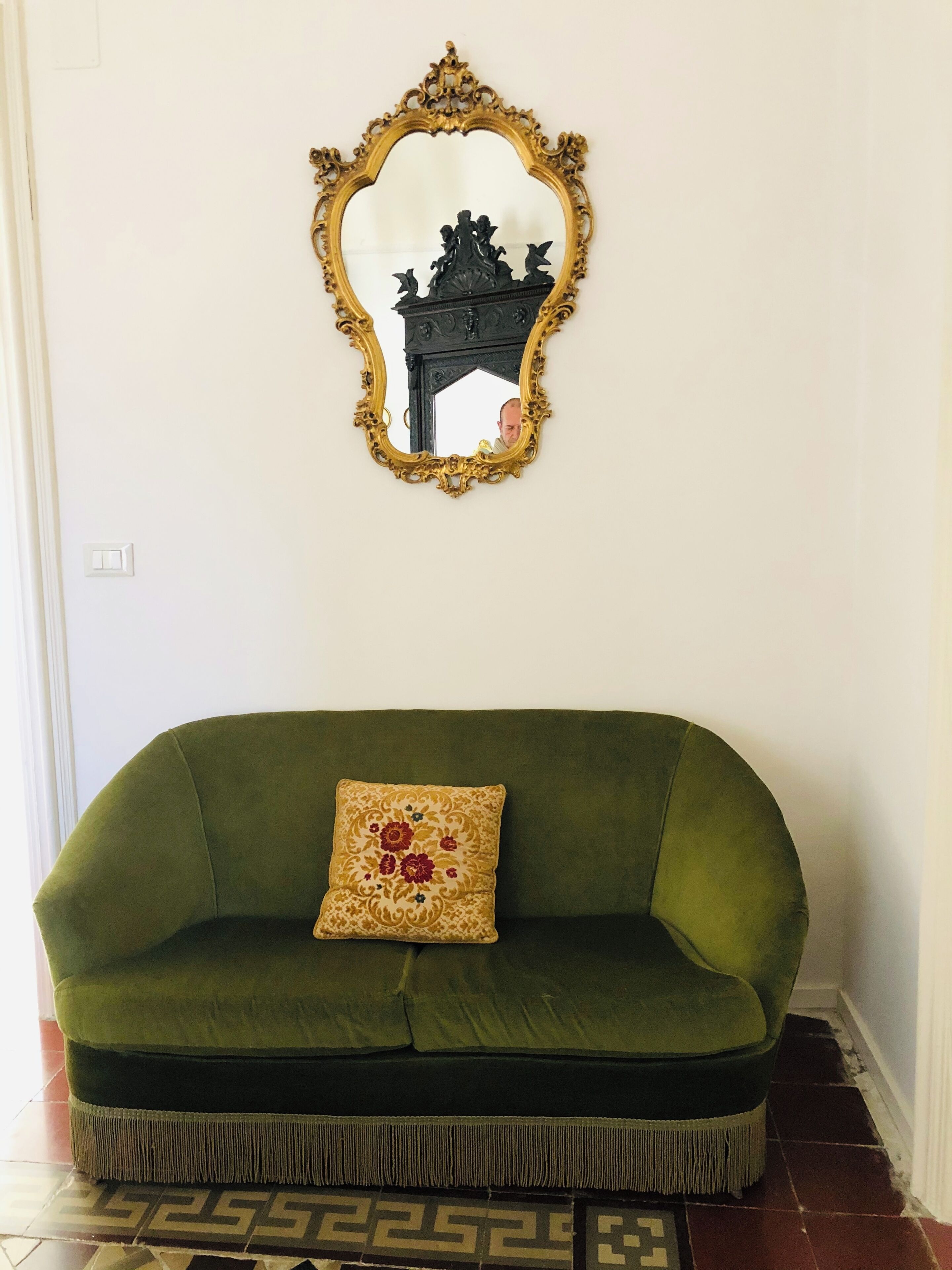 A green sofa with a decorative pillow and a gold-framed mirror on the wall.