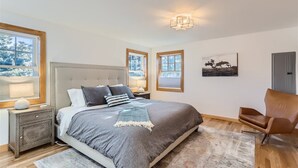 A bedroom with a large bed, two bedside tables, a chair, and a painting on the wall.