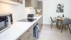 A modern kitchen with a microwave, toaster, and stove, a dining area with a table and chairs, and a wall-mounted artwork. - Exeter Cathedral Two-bedroom Stay (Exeter)