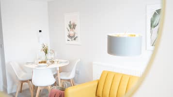 A modern dining area with a round table, white chairs, and a yellow sofa.