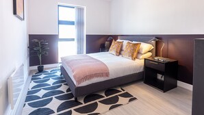 A modern bedroom with a bed, bedside tables, a lamp, a potted plant, and a window. - Victoria Square Two-bed Accommodation by Belvilla (Birmingham)