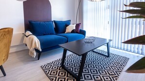 A modern living room with a blue sofa, a black coffee table, and a patterned rug. - Victoria Square Two-bed Accommodation by Belvilla (Birmingham)