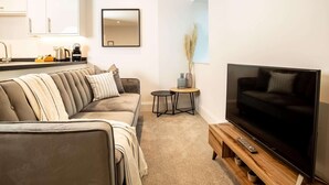 Ein modernes Wohnzimmer mit Sofa, Fernseher, Couchtisch und einer Küchenzeile im Hintergrund.
