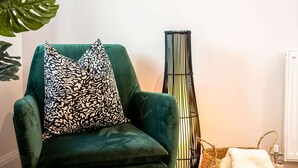 Ein grüner Sessel mit gemusterten Kissen, eine hohe schwarz-weiß gestreifte Vase und ein geflochtener Korb mit einem weißen Handtuch.