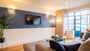 A modern living room with a flat-screen TV mounted on the wall, a glass coffee table, and a sofa with cushions.