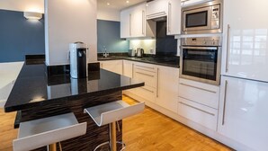 A modern kitchen with white cabinets, stainless steel appliances, a black countertop, and a wooden floor.