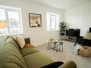 A modern living room with a green sofa, a small round table, a TV, and a large window. - One-bedroom Near Torquay Museum by Belvilla (Torquay)