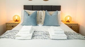 Una cama bien hecha con dos almohadas, dos lámparas de noche y un adorno en la pared.