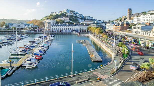 Un puerto deportivo con barcos amarrados, un paseo marítimo y edificios de arquitectura histórica.
