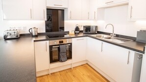Una cocina moderna con armarios blancos, encimera negra, horno empotrado, cafetera y tostadora.