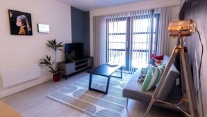 A modern living room with a flat-screen TV, a sofa, a coffee table, and a floor lamp. - One Bed Apartment Gem Steps to City by Belvilla (Birmingham)