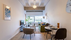 A modern living room with a sofa, chairs, a dining table, and a large window.