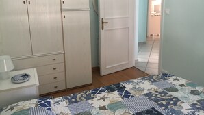 Een slaapkamer met een bed, een kledingkast, een nachtkastje en een deur naar een badkamer.