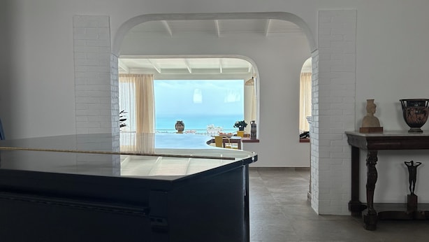 A spacious room with a piano, a view of the sea, and a white brick wall. - La casa di Pippo Flora (Agrigento)