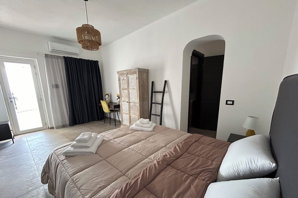 A bedroom with a large bed, a desk with a chair, a wardrobe, and a ladder.